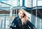 woman in black leather jacket sitting on red metal fence during daytime