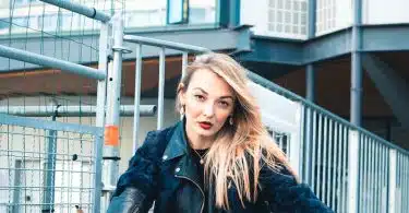 woman in black leather jacket sitting on red metal fence during daytime