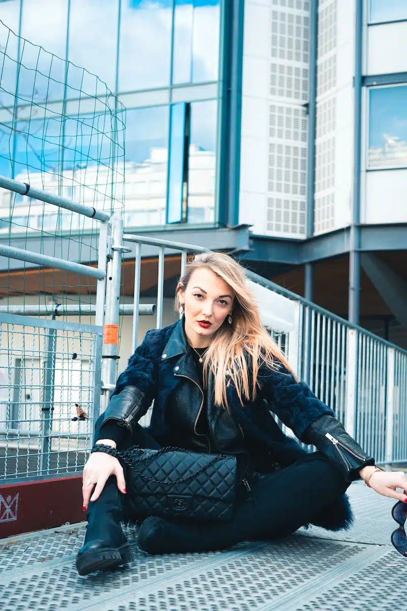 woman in black leather jacket sitting on red metal fence during daytime