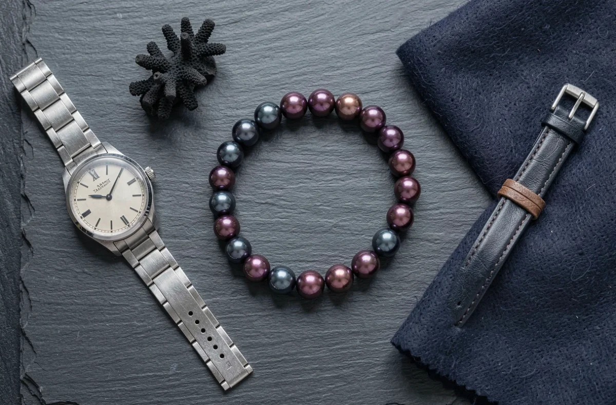 Bracelet en perles de Tahiti pour homme en flat lay avec montre vintage et accessoires masculins sur ardoise
