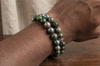 Bracelet perle de Tahiti pour homme porté au poignet, gros plan sur les reflets nacrés irisés vert et paon