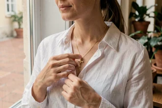 Femme portant une croix du Portugal en or sur une chemise en lin blanc dans un café de Lisbonne, style quotidien élégant